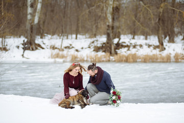 Fototapeta na wymiar Stylish beautiful young couple bride and groom, dog sitting on the background of a winter landscape river.