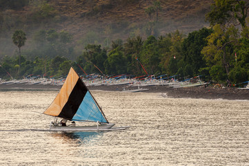 A Balinese Traditional Sailing Fishing Boat. A fishing boat, called jukung, returns to shore after night fishing to unload the catch in the early morning sunrise. Jemeluk, Amed, Bali is the location. © LoweStock