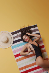 Fashion photo of beautiful and young lady in swimsuits posing in studio, is resting on a colorful towel