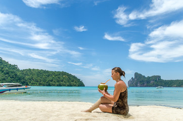 Panorama of Phi Phi bay. Young beautiful woman drinking coconut water on tropical beach of Phi Phi Don island, Thailand. Vacation concept.