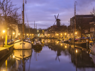 Dutch old city Schiedam landscape during calm weather with reflections in a canal, old barges and windmill