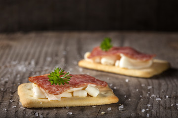 Cracker snacks with square salami and cheese cream