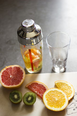    kiwis, grey fruits and oranges together with a shaker and a glass on a dark lit background.