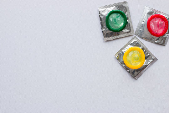 Three colored condom on white background with space for text