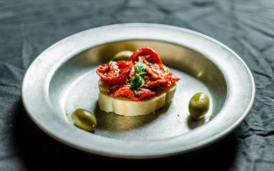 Close up of Spanish tapas sandwich with sun dried tomatoes, olives, and basil against back background. Selective focus