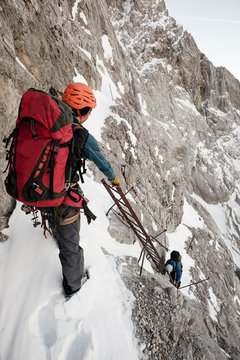 Two mountaineers climbing steep wall on safety ladder
