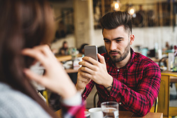 Man at cafe bar, taking a photo of his girlfriend.
