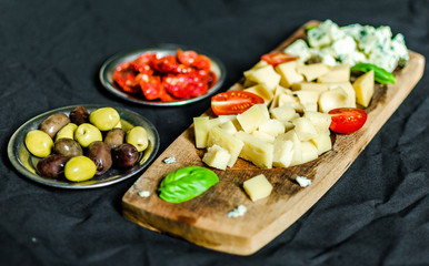 Close up of Italian cheese antipasti delicatessen platter against black background. Selective focus