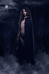 Beautiful gothic girl in a black cloak against a nightscape