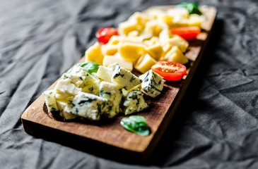 Close up of Italian cheese antipasti delicatessen platter against black background. Selective focus