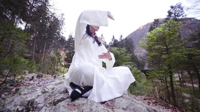 Woman on big rock sit make QiGong exercise form with hands 4K
