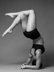 Young beautiful woman performing headstand against gray background, black and white