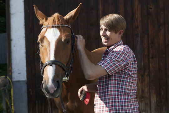 Man brushing horse with brush on ranch