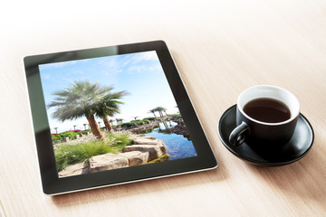 Tablet computer with sea view picture, on the desk with a cup of coffee. Travel motif wallpaper