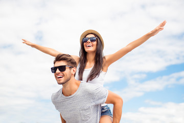 Young guy piggybacking cheerful girlfriend like airplane on the