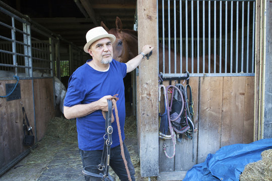 Senior man in front of stable holding horse's bridle