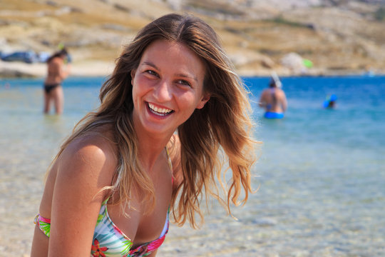 Beautiful tanned girl in a bikini sitting on a rocky beach.