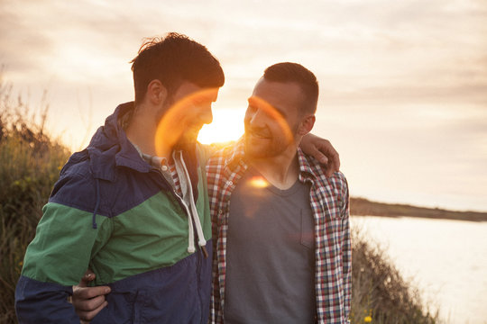 Two friends on water's edge embracing at sunset