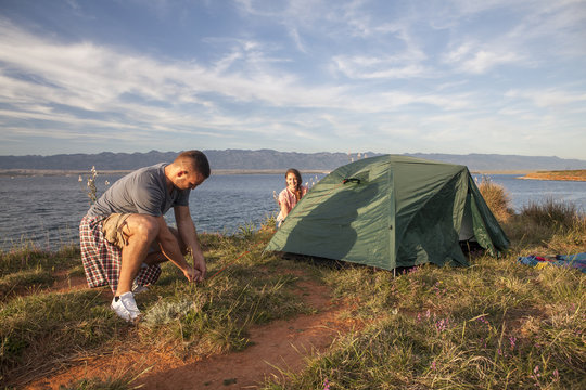 Young couple building up tent on water's edge