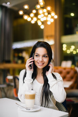 Young woman at cafe drinking coffee and talking on mobile phone