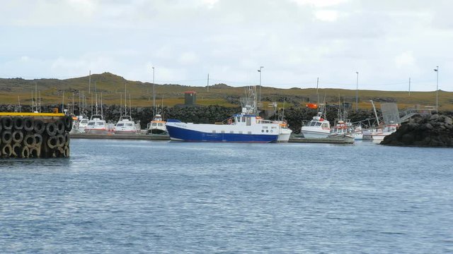 view of moored fishing boats, Atlantic waves are on first plan, tipical icelandic landscape