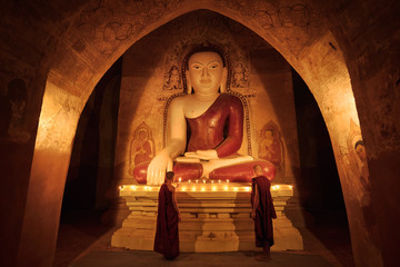Little monk praying with candles in front of buddha statue inside old pagoda, Bagan Myanmar
