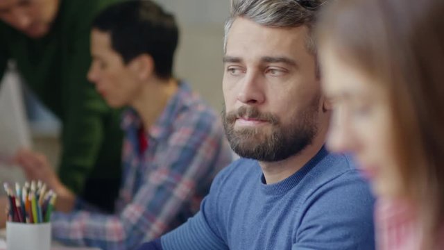 Rack focus with close up of attractive working businesswoman and her bearded colleague having a chat, coworkers discussing project in background 
