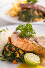 A decorating nice dish of salmon steak and beef served with mashed potato,lemon, saute spinach and sauce on background with wooden utensils.