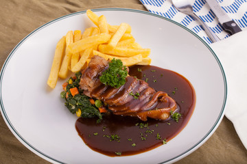 A nice dish of roasted duck breast confit in orange sauce served with fries on the table