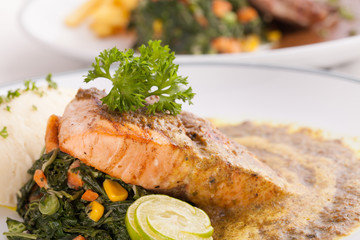 A decorating nice dish of salmon steak and beef served with mashed potato,lemon, saute spinach and sauce on background with wooden utensils.