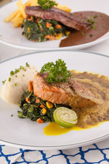 A decorating nice dish of salmon steak and beef served with mashed potato,lemon, saute spinach and sauce on background with wooden utensils.