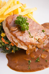 a dish of pork sirlion steak served with brown sauce and saute spinach and french fries in a nice dish.