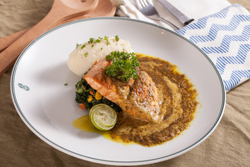 A decorating nice dish of salmon steak and beef served with mashed potato,lemon, saute spinach and sauce on background with wooden utensils.