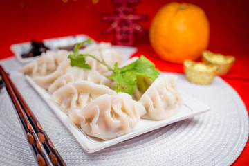 Chinese Jiaozi new year food with sauce and white placemat on red background. People will eat Jiaozi during Chinese New Year.It means earning more money.The Chinese text is "spring".