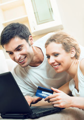 Young happy smiling couple with laptop, paying by credit card in internet store, at home