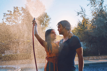 Couple having fun pour each other with garden hose