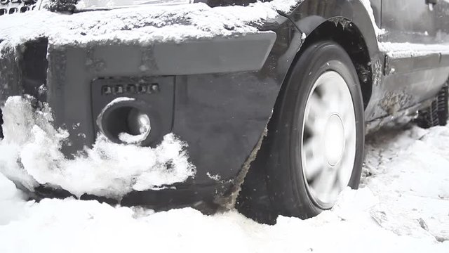 Color footage of a car's wheel being stuck in snow, and spinning.
