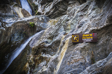 Warning Sign dangerous climbing at waterfall with stones in fore