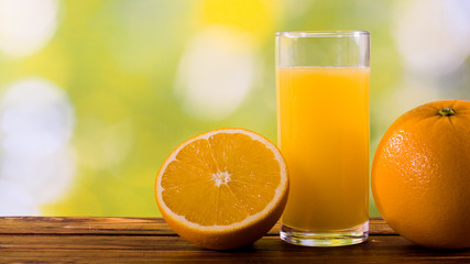 Orange juice in glass and oranges outdoors on wooden table