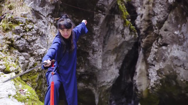 Concentration training pose with sword in traditional kimono under rock wall 4K
