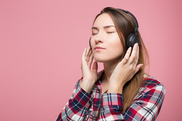hipster girl listening to the music in headphones over pink background isolated