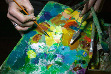 hands of artist mix paints on a palette. composition on a dark background 