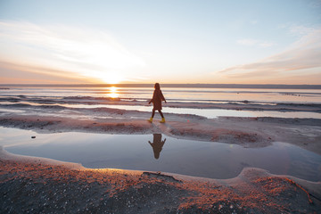 Beautiful girl is standing on the sea in a Sunbeam, yellow boots, long black coat, sand underfoot