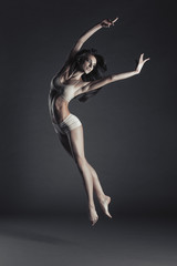 Young beautiful slim dancer jump on a black studio background.