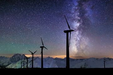 Silhouettes of wind turbines in the background of mountains and the starry sky