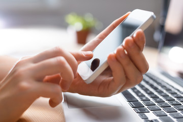 Finger pointing to phone screen, laptop in the bachground, informal business atmoshere