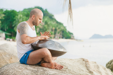 Man is sitting on the stone and playing hangdrum