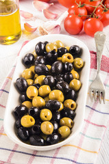 white bowl with oily green and black olives, tomato background,