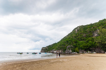 People Walking on the Beach with Cloudy Sky and Mountain.