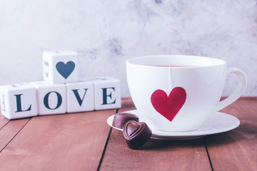 Valentine's day. Cup of tea and two chocolate candies in shape hearts. Message love spelled in wooden blocks. Love or holiday concept. Copy space